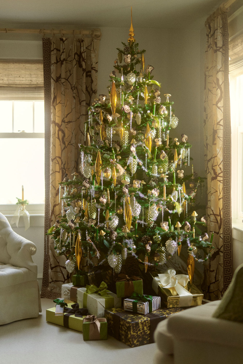 A decorated Christmas tree in a living room setting, adorned with gold and silver ornaments, wrapped in green and gold ribbons, with presents underneath.