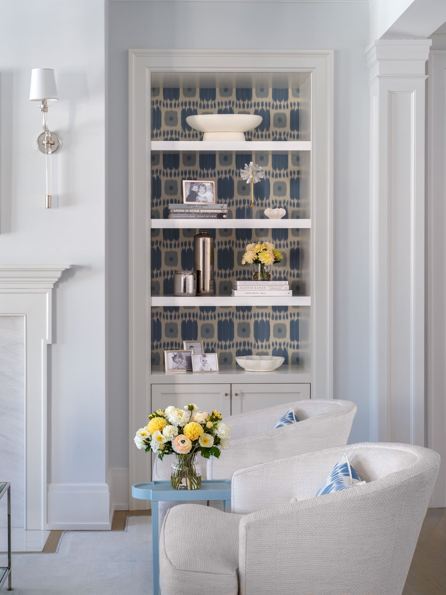 Living room with a bookshelf, floral arrangements by Diane James Home, and white armchair.