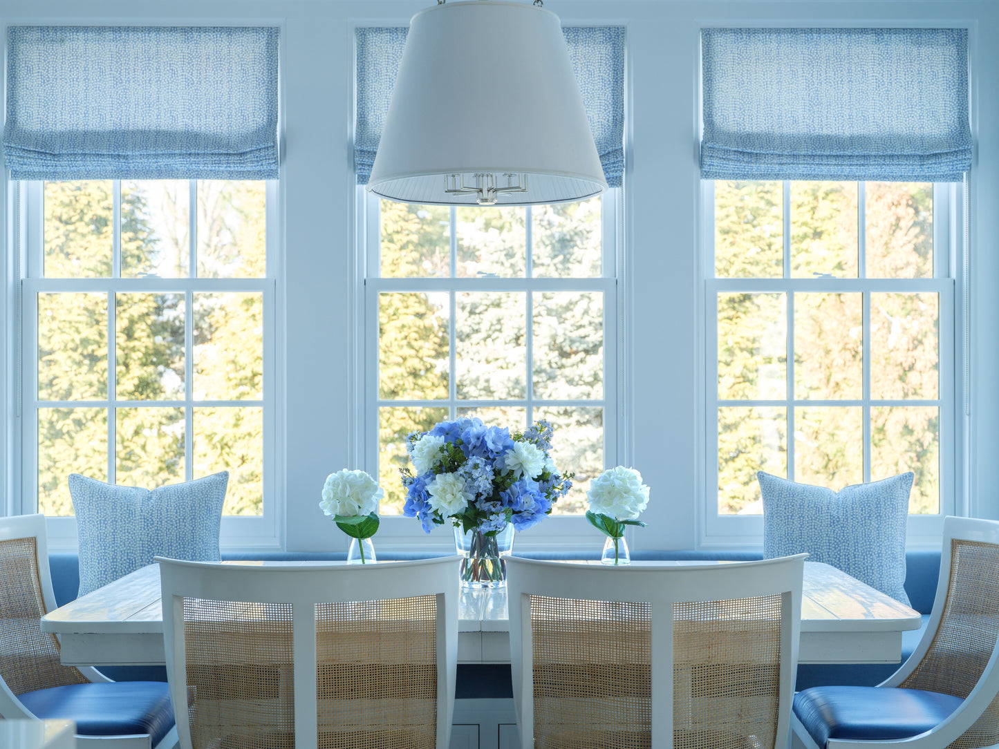 Dining room with a table, chairs, and faux floral boquuets by Diane James Home in front of large windows.
