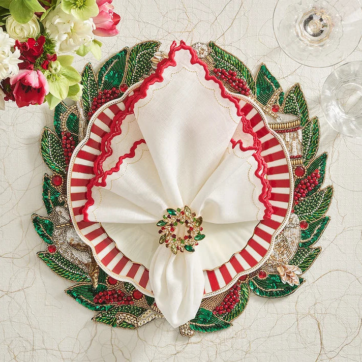 Decorative napkin ring with white fabric, red and green embellishments on a textured surface with flowers and glasses.