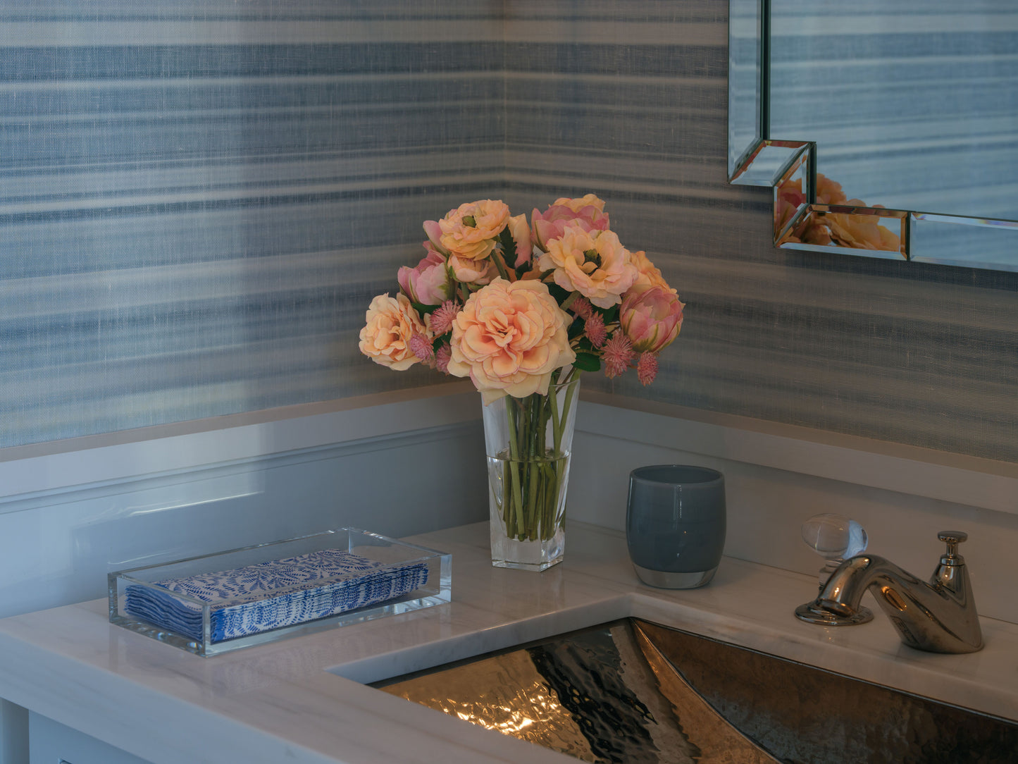 Bathroom counter with a bouquet of faux flowers by DIane James Home and a tray against striped wallpaper.