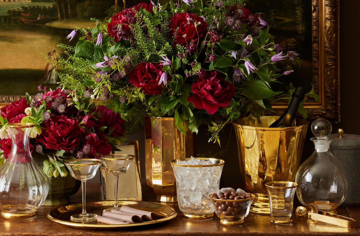 Decorative table setting with flowers, glasses, and a ice bucket on a wooden surface.