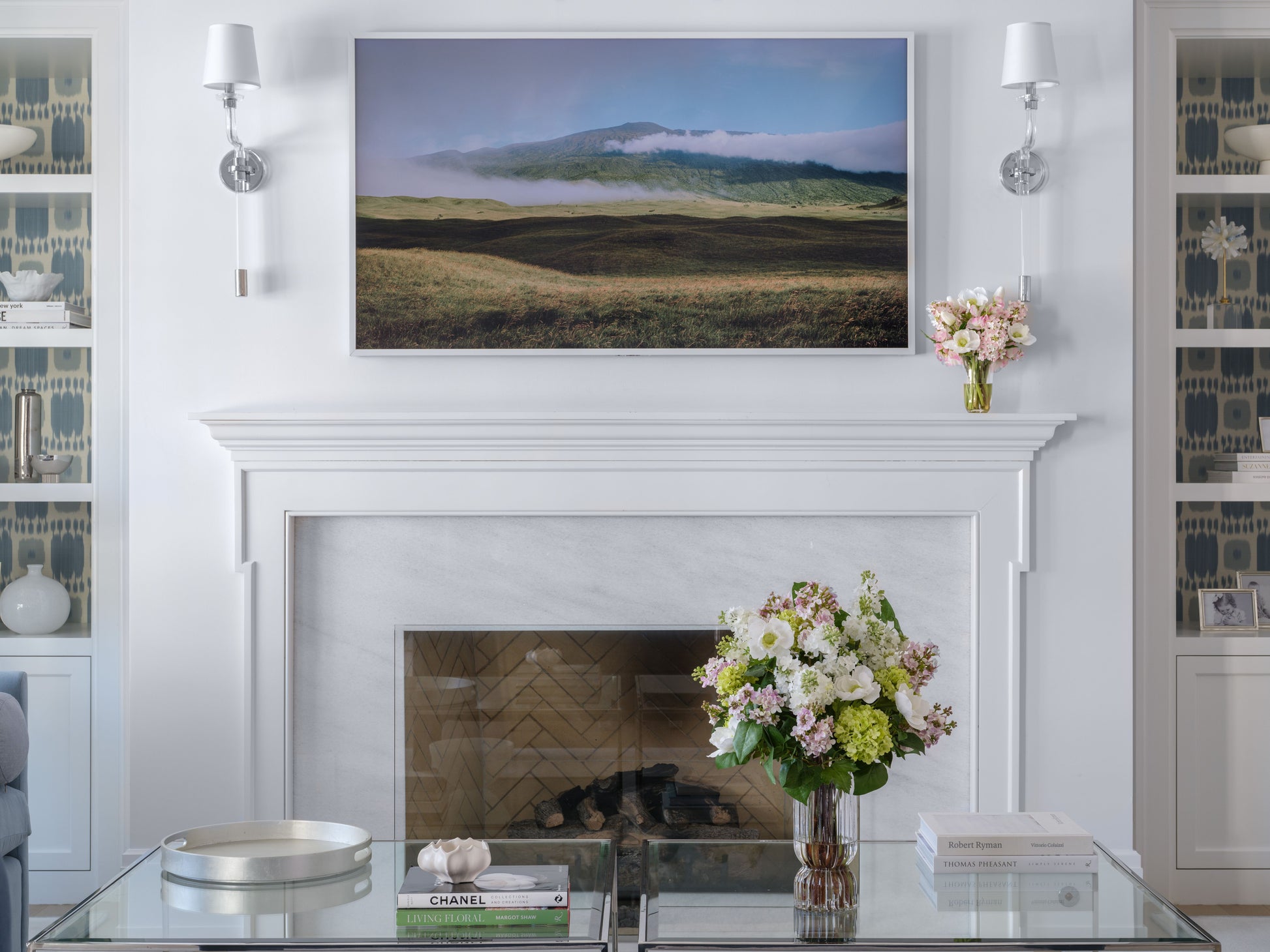 Living room with a fireplace, artwork above, and floral arrangements by DIane James Home on a table and mantle.