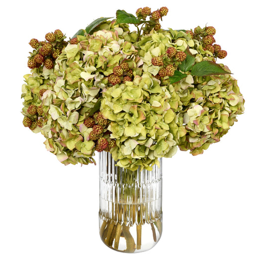 A large artificial hydrangea bouquet by Diane James Home in a ribbed clear glass vase, featuring muted green and  hydrangeas and wild raspberries and green leaves, isolated on a white background.