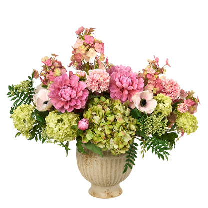 Caledonia is a vibrant artificial flower centerpiece in a distressed cream-colored ceramic urn created by Diane James Home. The luxury bouquet features prominent, pink dahlias, light green hydrangeas, pale pink anemones, and green foliage, all set against a solid white background.
