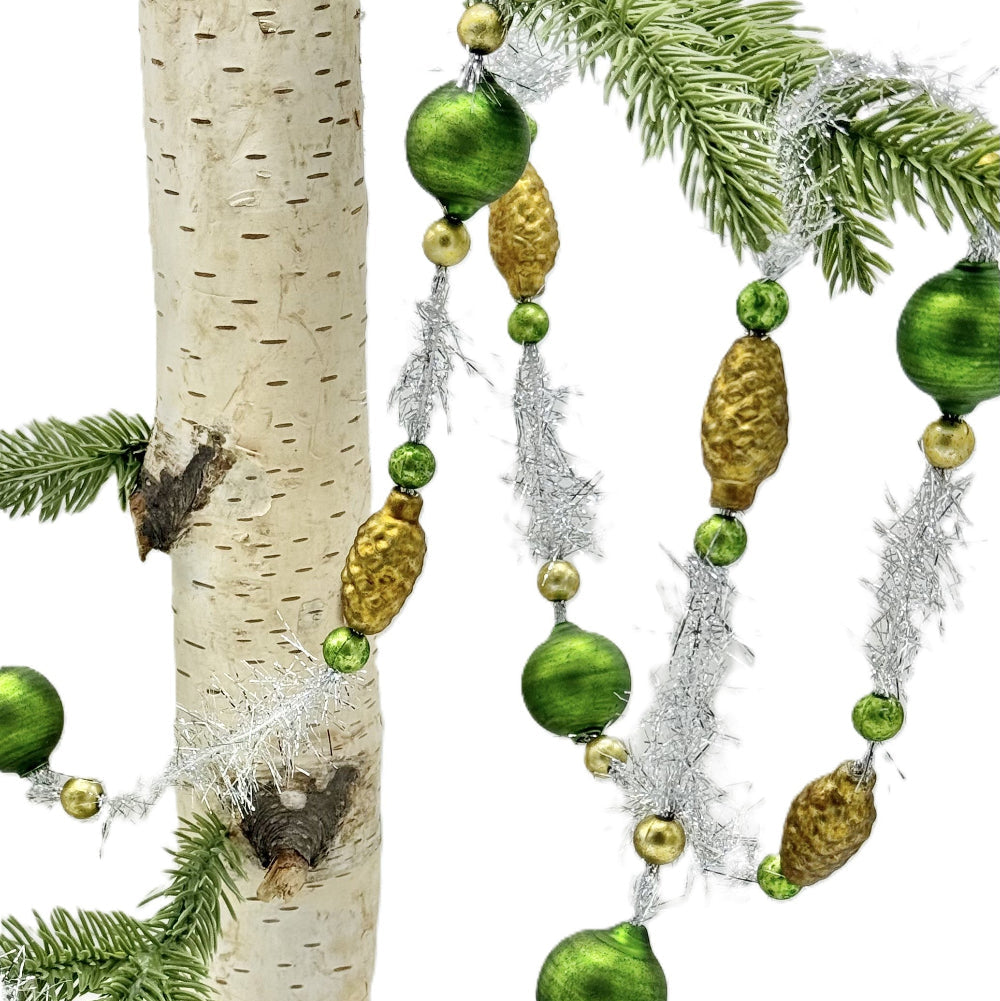 Green and gold Christmas tree garland with shiny green beads, textured gold pinecones, and silver tinsel draped over pine branches and a birch tree trunk on a white background.