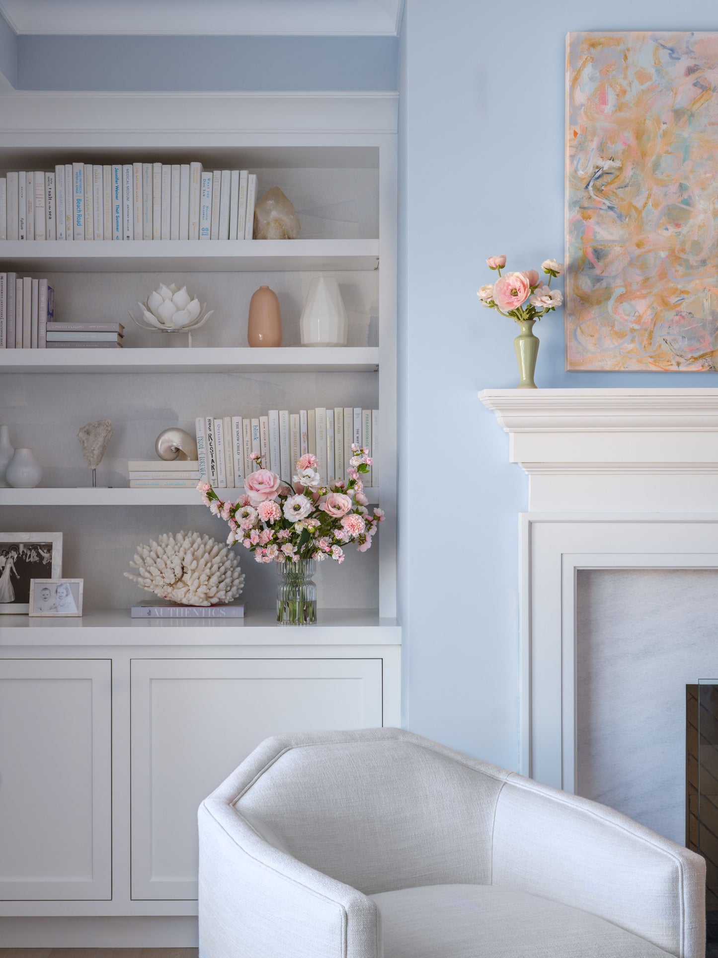 Living room with white bookshelf, floral arrangements by Diane James Home, and a fireplace.