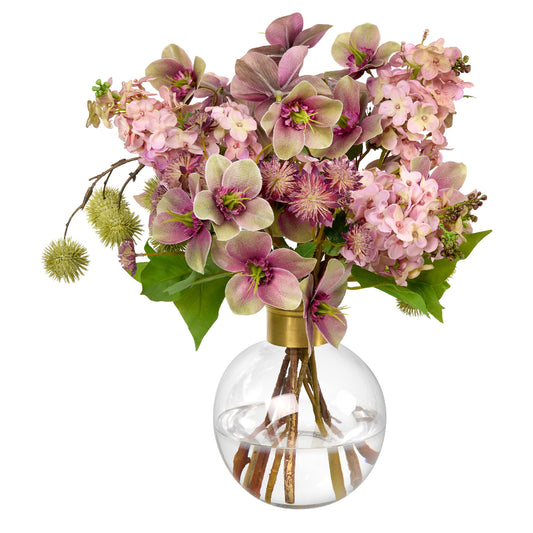 An artificial floral arrangement by Diane James Home featuring pink and lavender hellebores and lilacs with green leaves, styled in a clear glass globe vase with a gold collar, set against a solid white background.