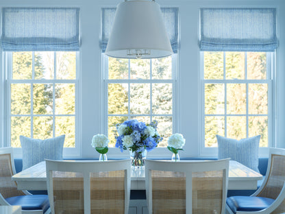 Dining room with a table, chairs, and faux floral boquuets by Diane James Home in front of large windows.