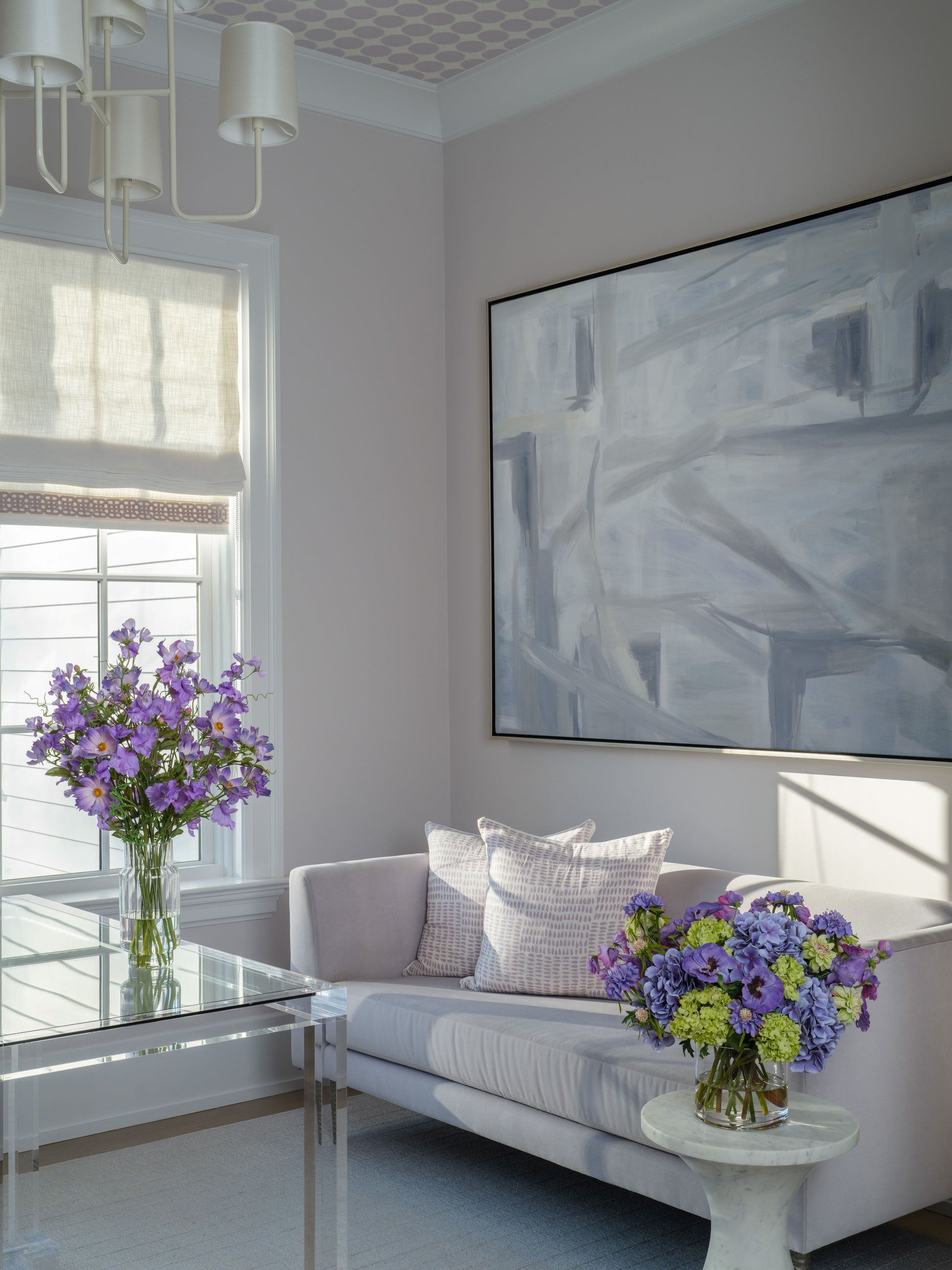 Modern living room with a gray sofa, abstract painting, and faux floral arrangements by Diane James Home