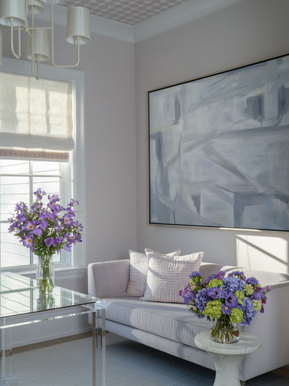 Modern living room with a gray sofa, abstract painting, and faux floral arrangements by Diane James Home