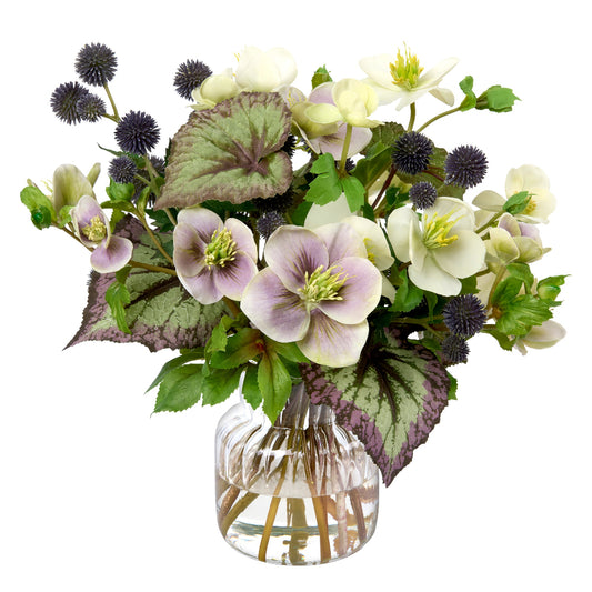 A mixed faux floral arrangement by Diane James Home in a clear glass vase on a white background, featuring pale purple and white hellebores with green and burgundy begonia leaves, plus dark purple globe thistles.