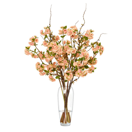 Artificial peach blossom branch with pink flowers in a clear vase on a white background