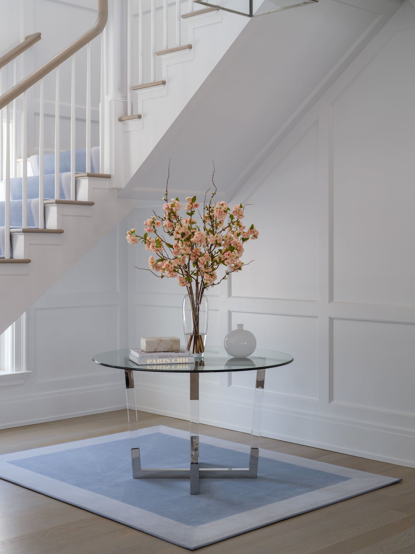 Modern interior with a glass table, vase of flowers by Diane James Home, and staircase in the background.
