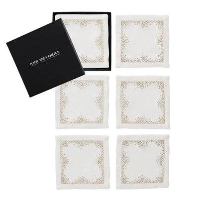 Set of six white cocktail napkins with gold border design in a black Kim Seybert box on a white background