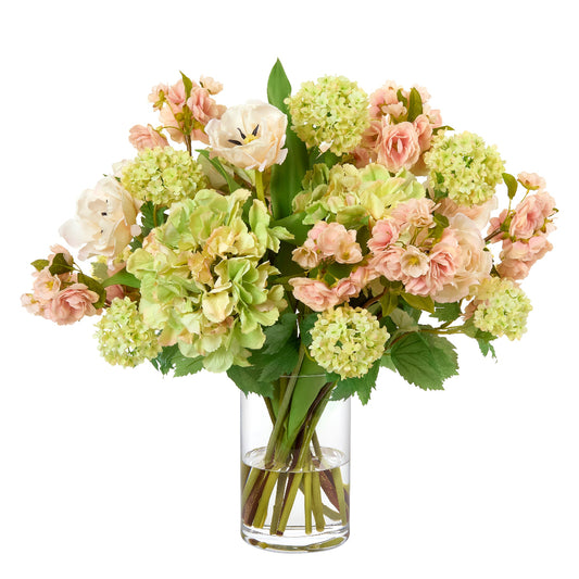 Bouquet of faux hydrangeas, snowball viburnum, tulips, and peach blossoms in a clear vase on a white background