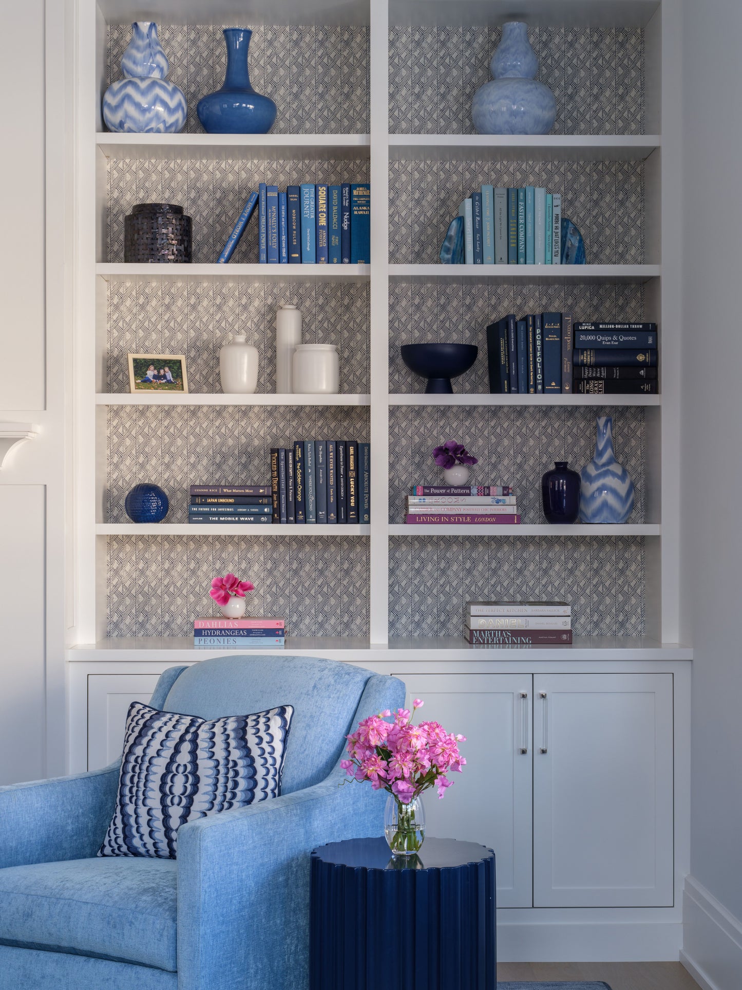 Blue armchair in front of a bookshelf with decorative items including faux florals by Diane James Home