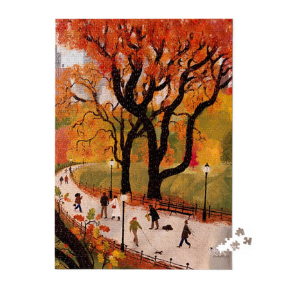 A completed jigsaw puzzle showing an autumn park scene with large black trees, orange and yellow foliage, a winding path, lampposts, and small people walking dogs and strolling. A small cluster of loose puzzle pieces sits at the lower right on a white background.