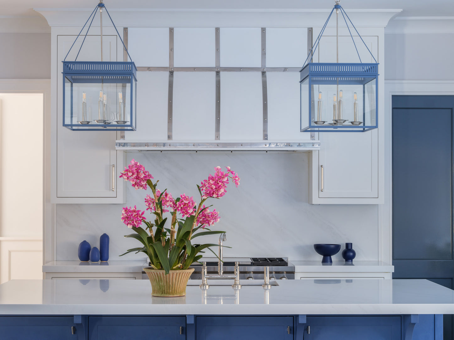 Modern kitchen with blue pendant lights, white cabinets, and a pinkfaux orchid arrangement by Diane James Home on the counter.